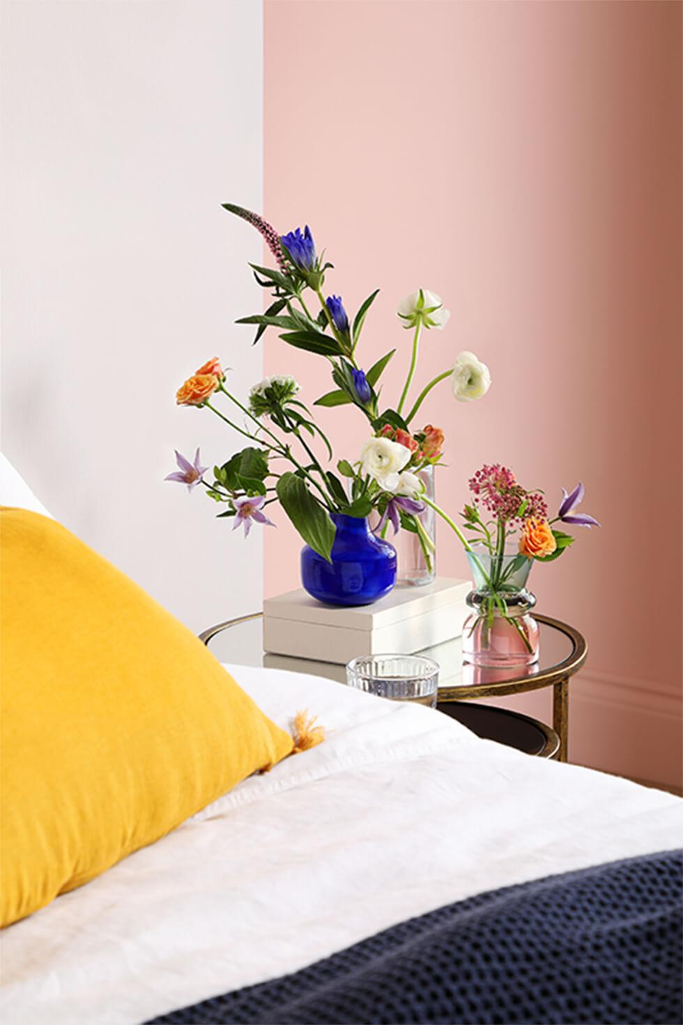 Spring floral arrangement in a blue vase by a bedside, in a pastel pink and yellow bedroom