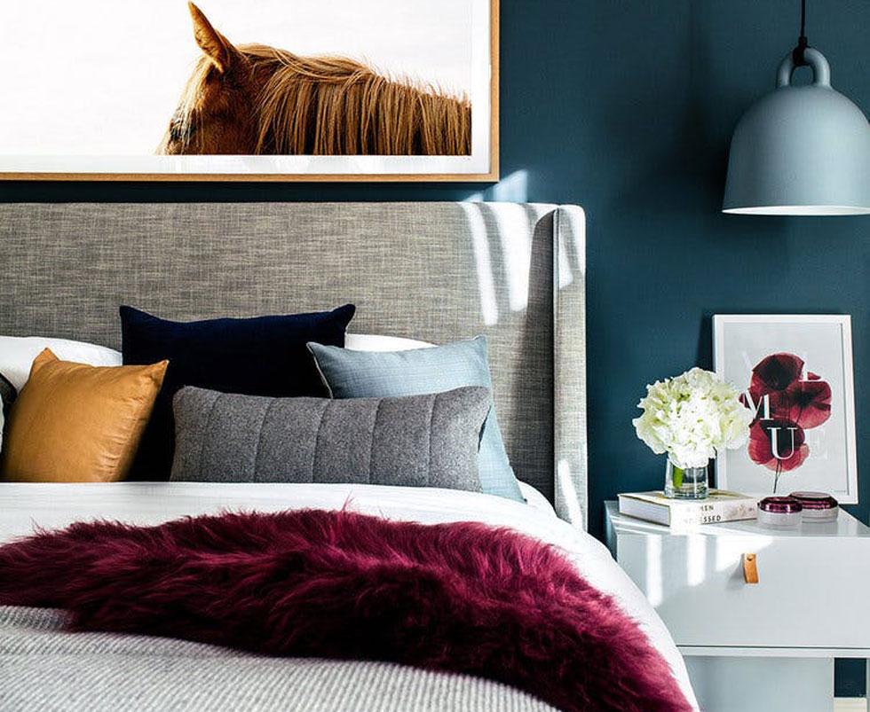 Bedroom with burgundy fur throw, teal wall and ochre pillow. 