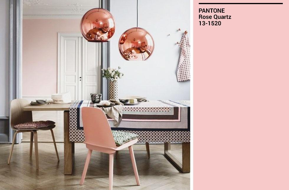 A dining room with a pink chair, wooden table, and rose gold lamps.