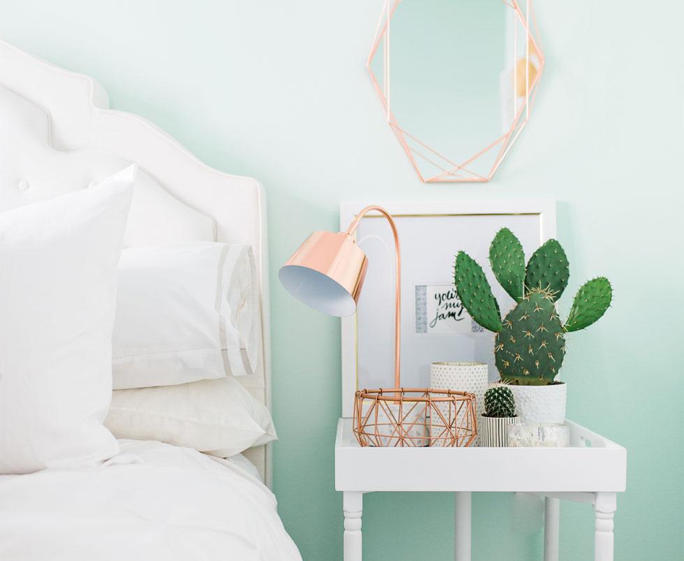 A white bedroom with a pink lamp and a cactus. 