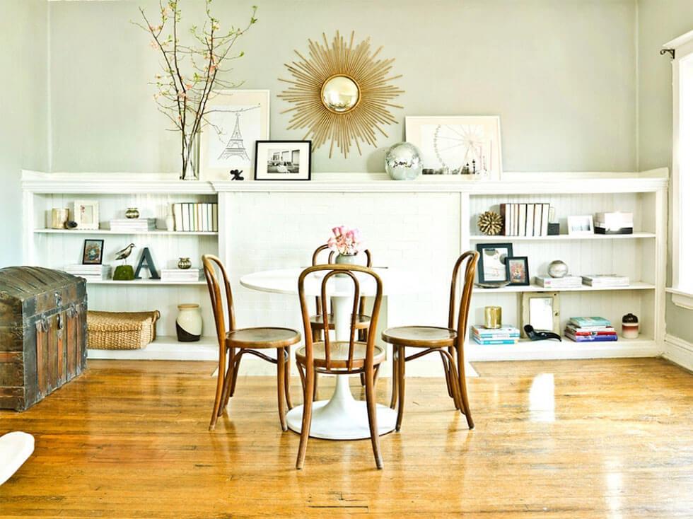 Art deco, baroque inspired dining room with wooden floors, a sunburst mirror and airy space.