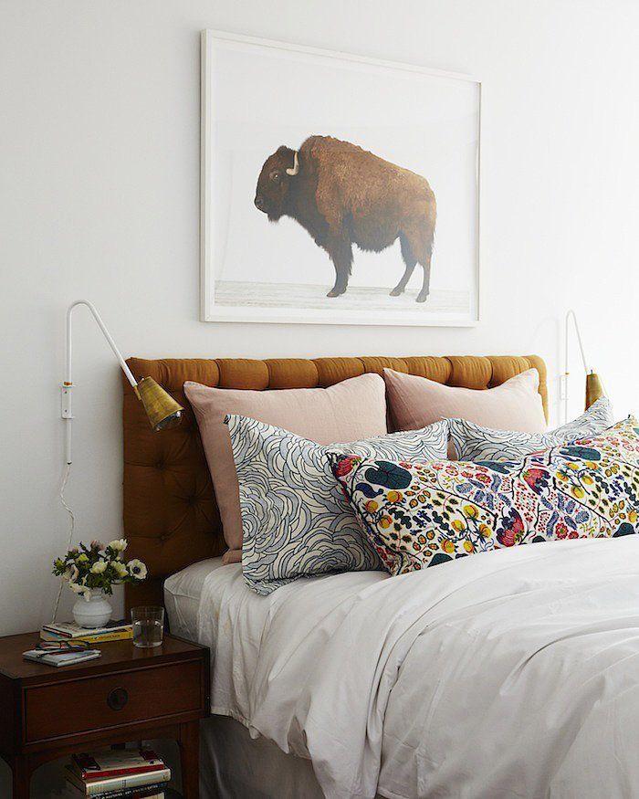 A bedroom with white sheets, a brown headboard, colourful pillows, and a bison photograph on the wall.