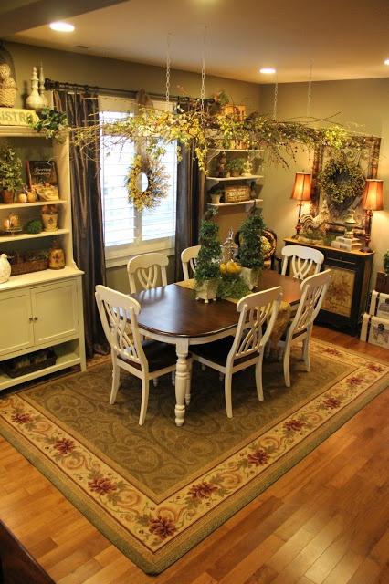 A dining room with a wooden table with white legs, and matching white chairs, with a carpet and lots of plants.
