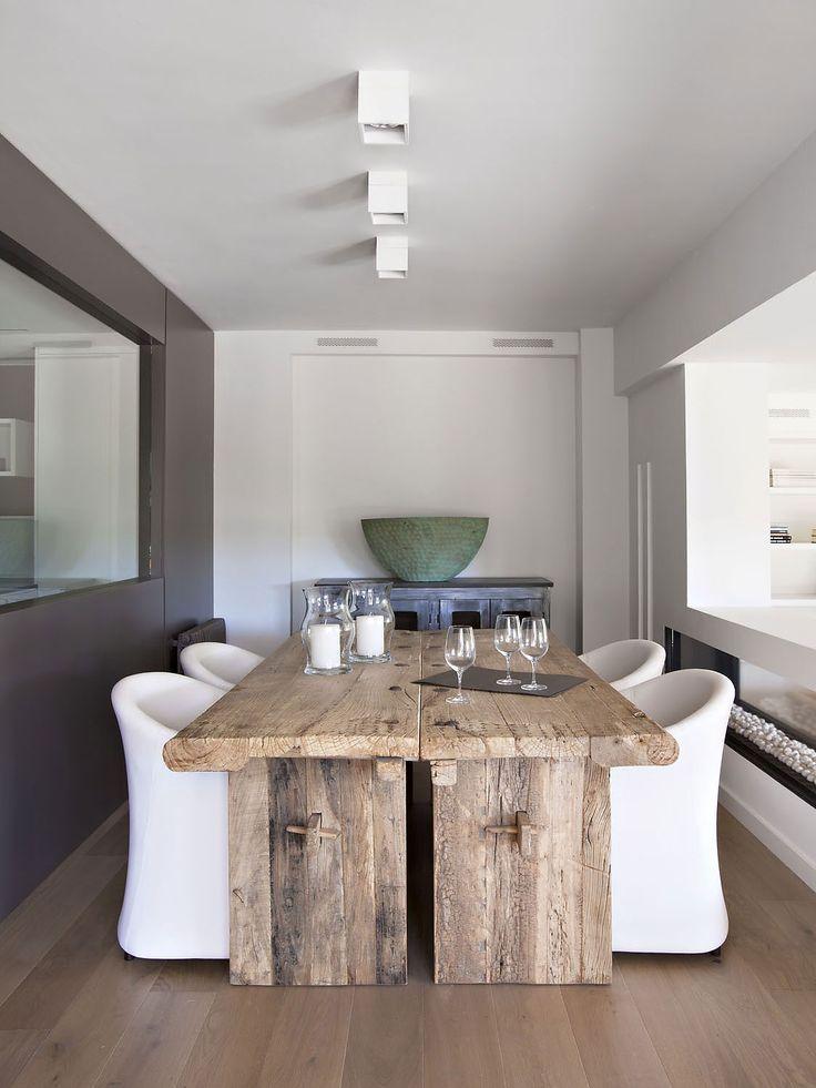 A dining room with a solid, large wooden table and white modern chairs.