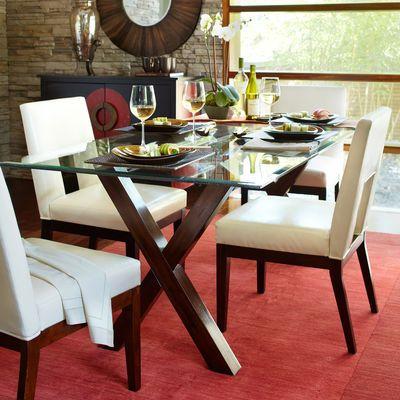A glass dining table, with wooden legs, white chairs, on a red carpet.