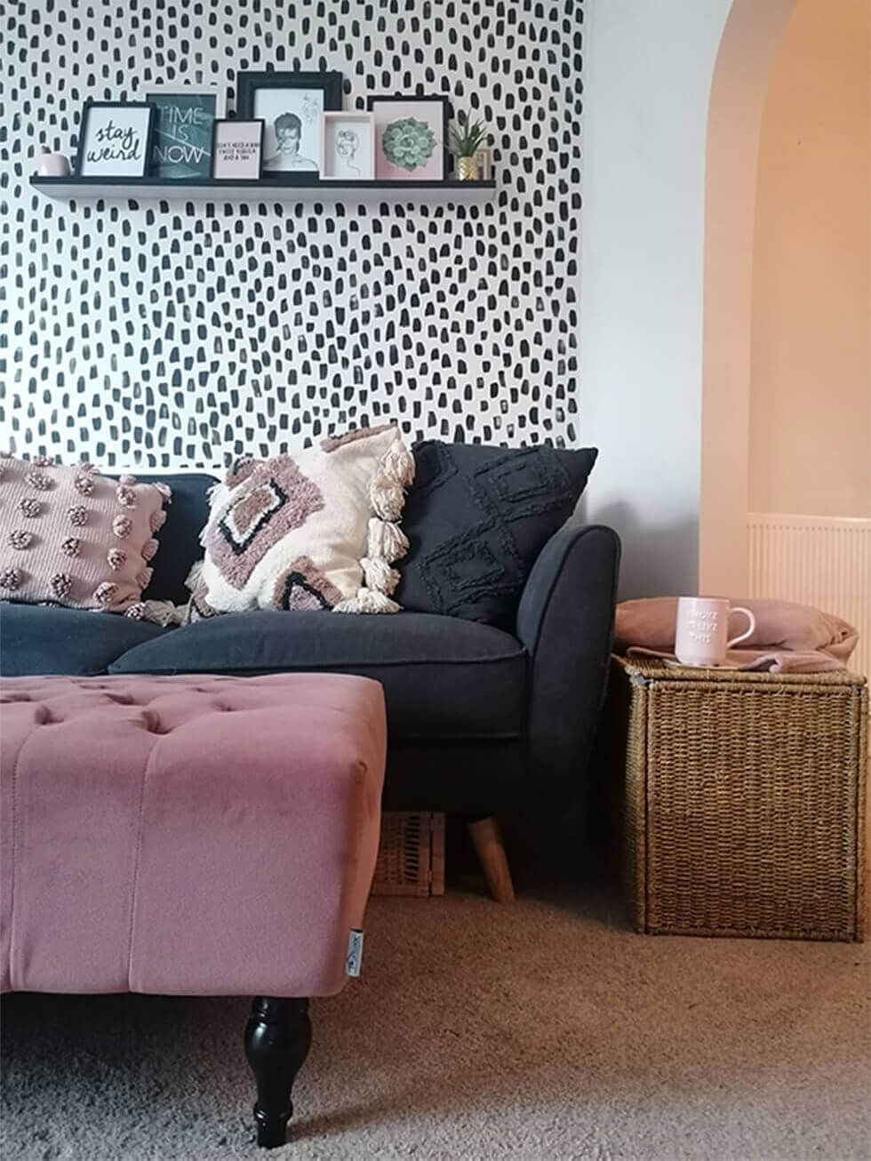 Black sofa and pink ottoman in a living room with polka dot walls