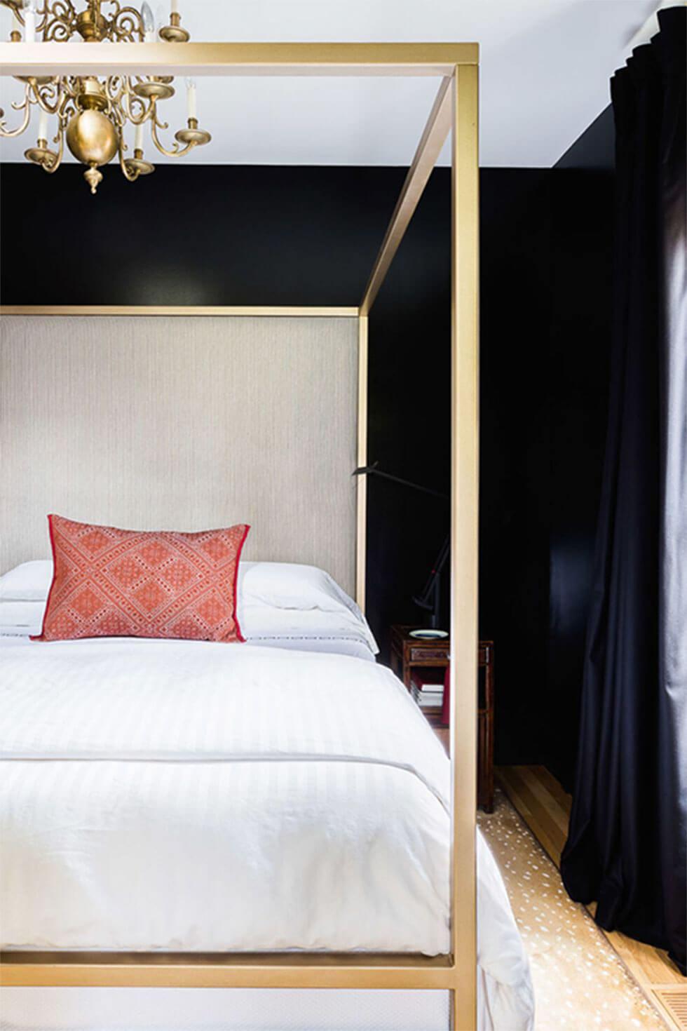 Black and white bedroom with a bronze four poster bed and chandelier, and pink cushion