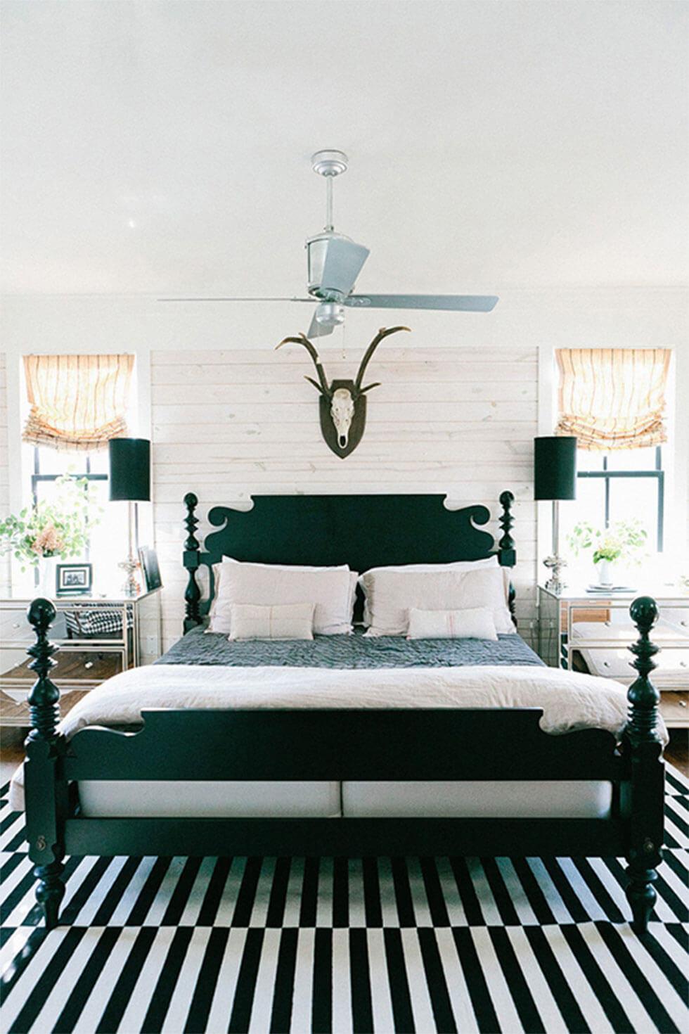 Classic black wooden bed in a white brick room with black lamps and modern, printed rug