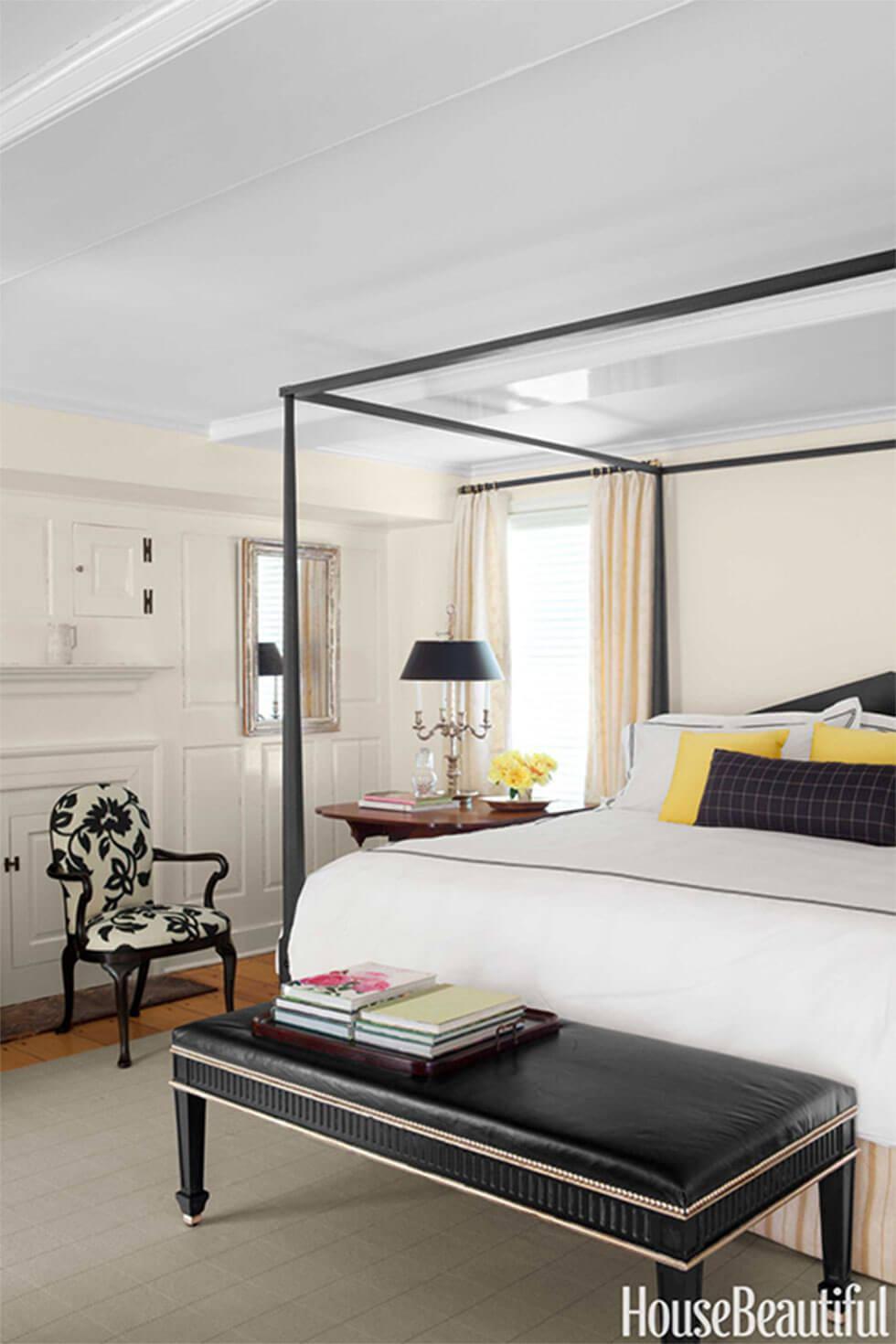 Classic black and white bedroom with floral armchair, four poster bed and bright yellow cushions