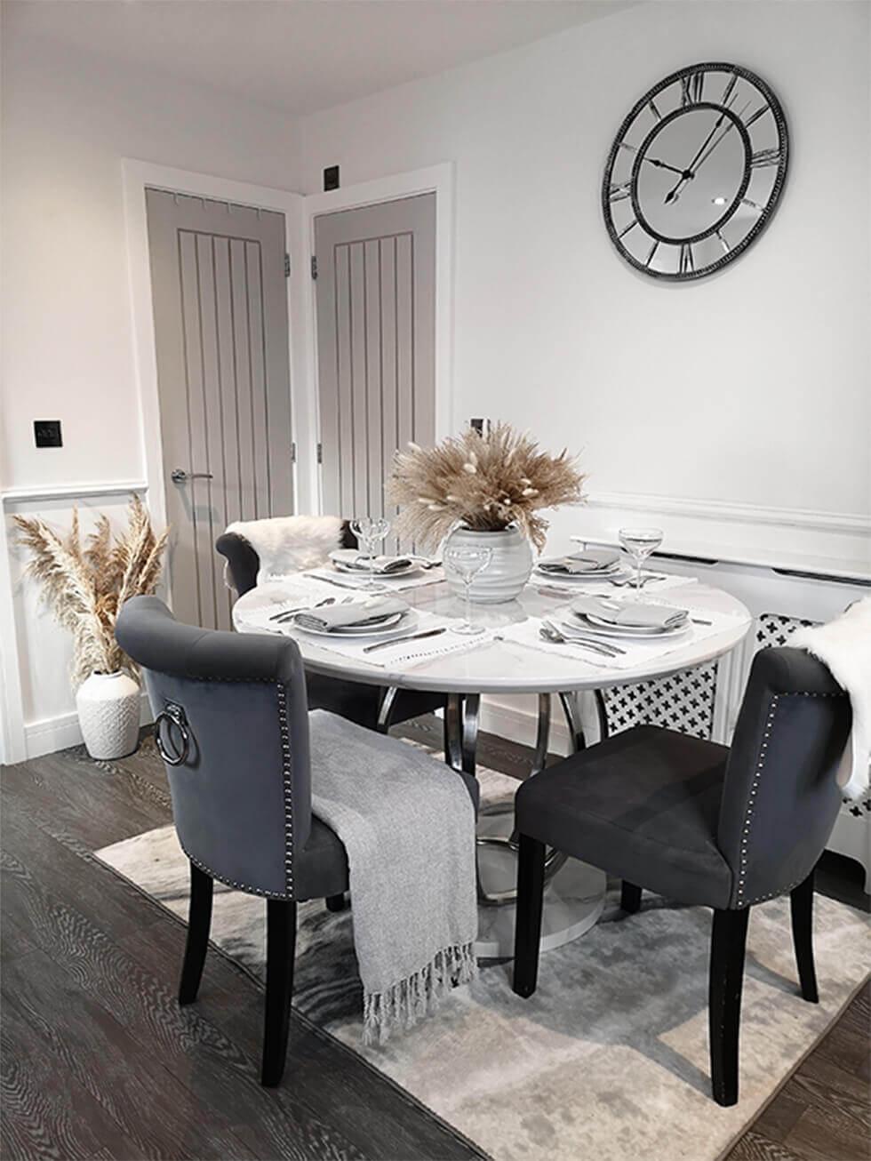 Open plan dining space with round marble table, grey fabric dining chairs and grey doors