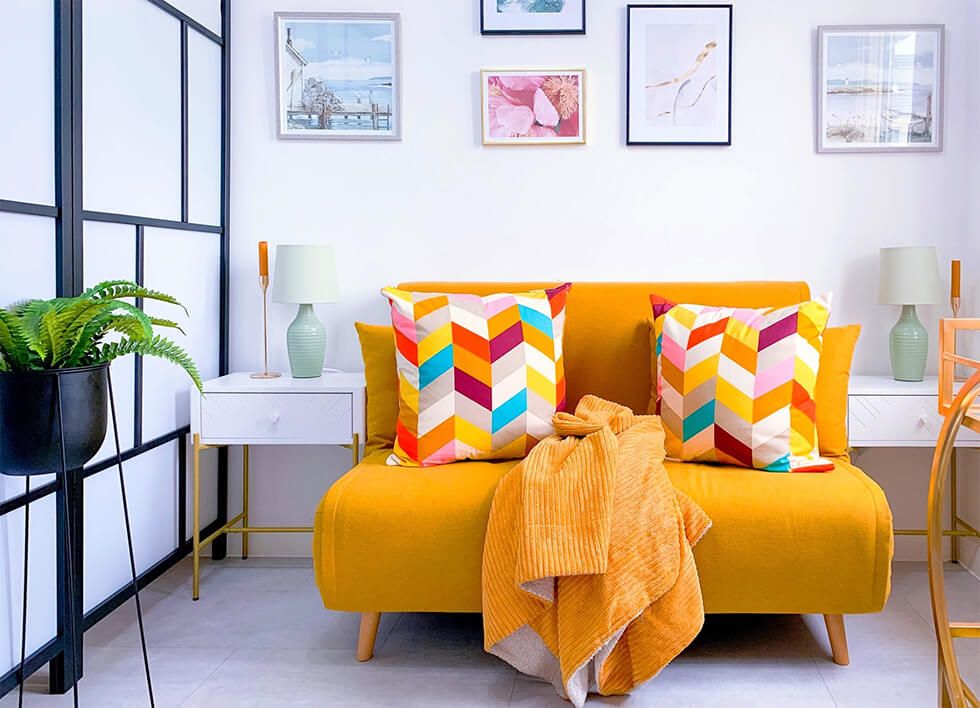 White living room with a mustard sofa decorated with colourful cushions