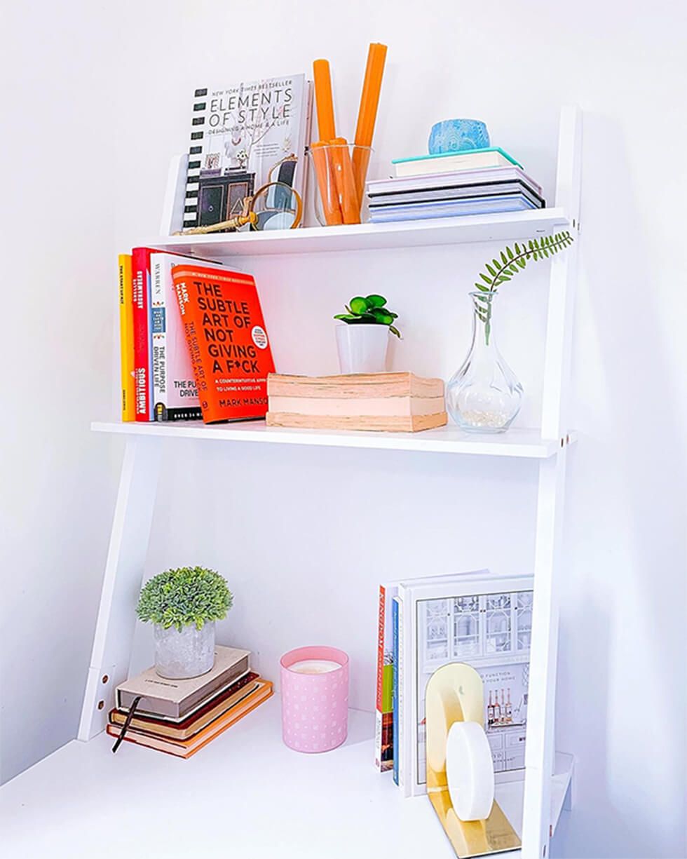 White shelf arranged neatly with colourful books and small plants