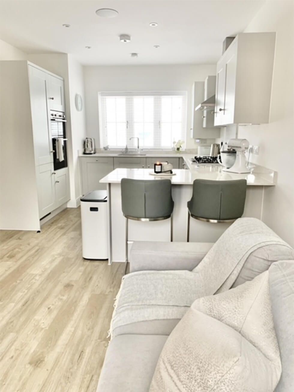 Modern all-white kitchen with a breakfast island, bar stools and sofa next to it