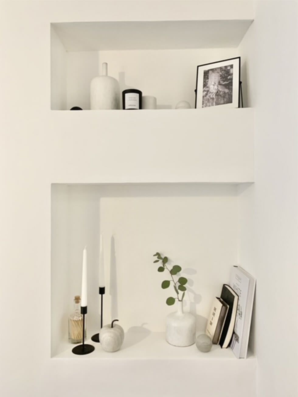 Minimalist wall niche decorated with candles, vases and books