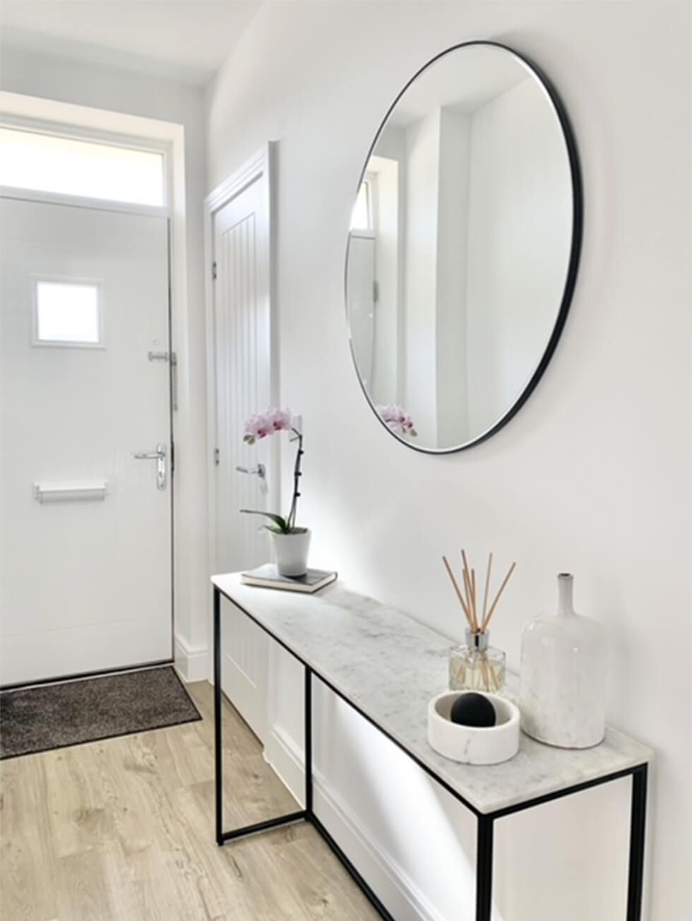 An entrance console table with a potted orchid, large round mirror and scent diffusers