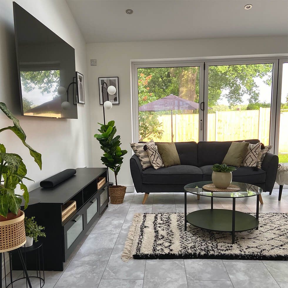 A neutral living room with black furniture, textured beige accessories and potted plants