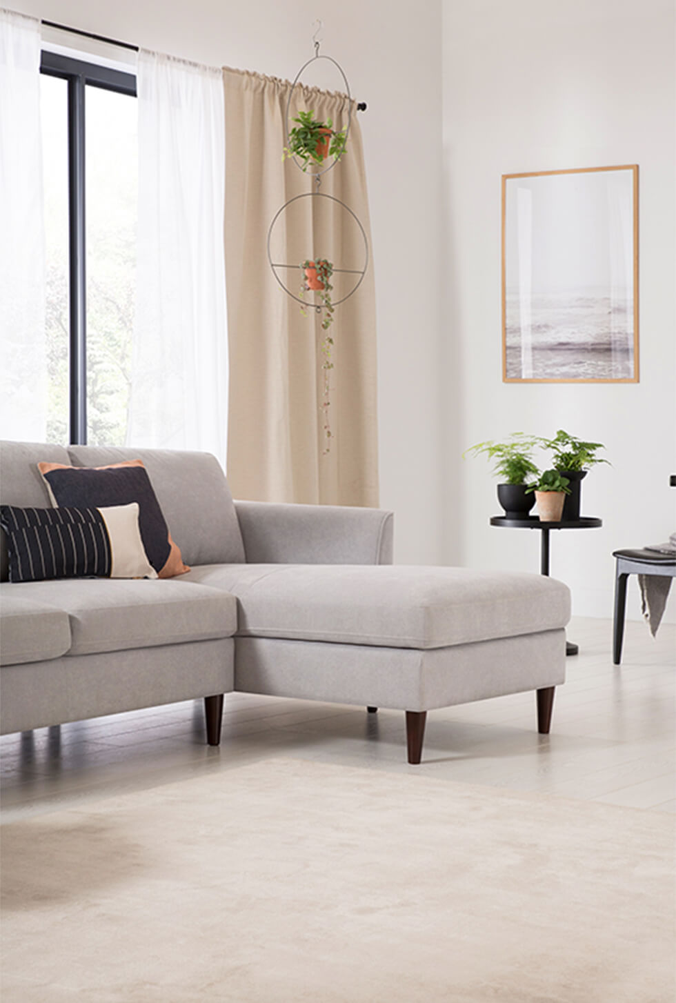 Grey plush fabric corner sofa in a modern white living room with indoor plants