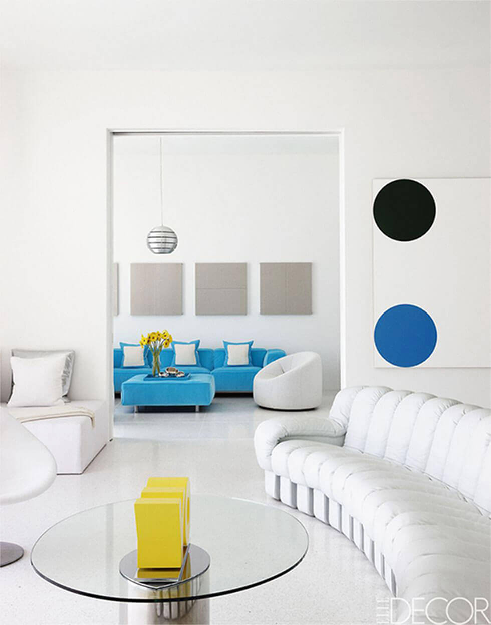 An all-white living room with vibrant pops of yellow and blue.