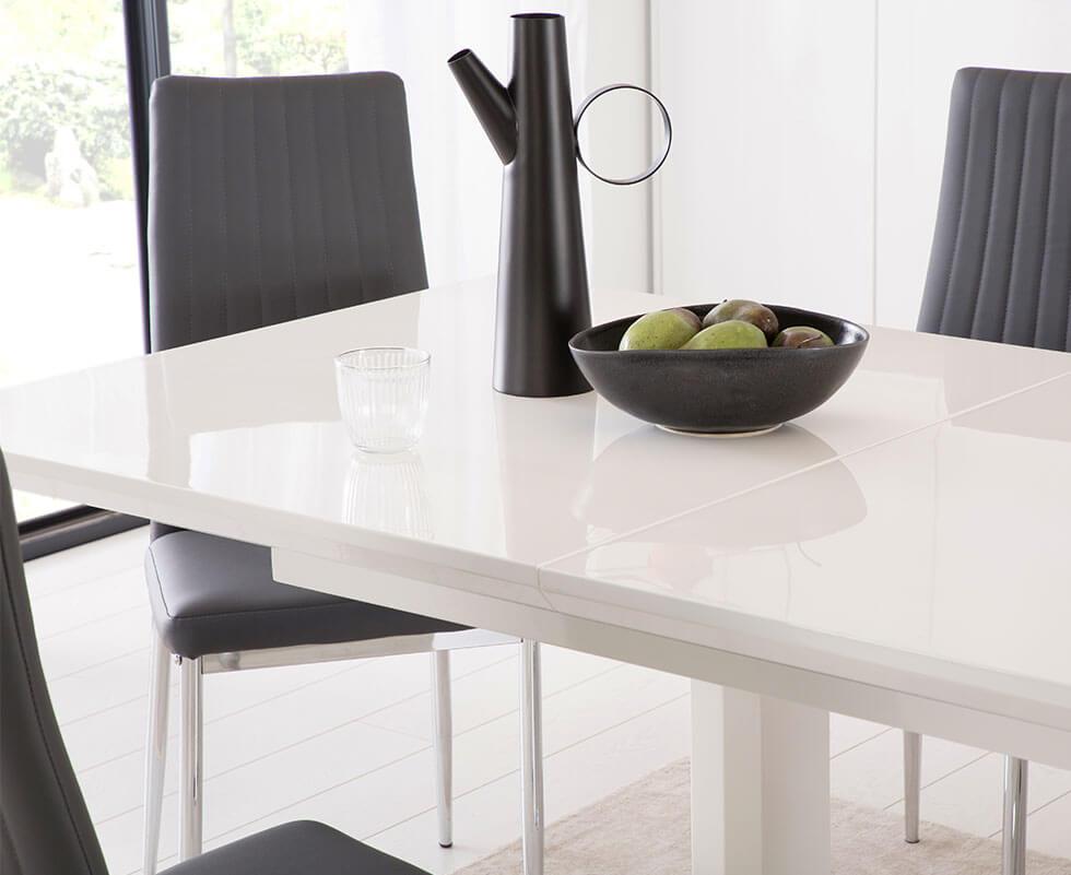 High gloss white table with black leather chairs with chrome legs in a simple, neutral dining room.