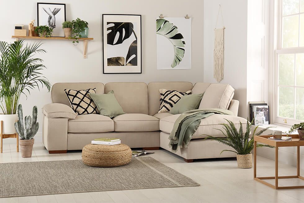 A relaxing living room with a beige linen corner sofa, green cushions, plants and natural artwork