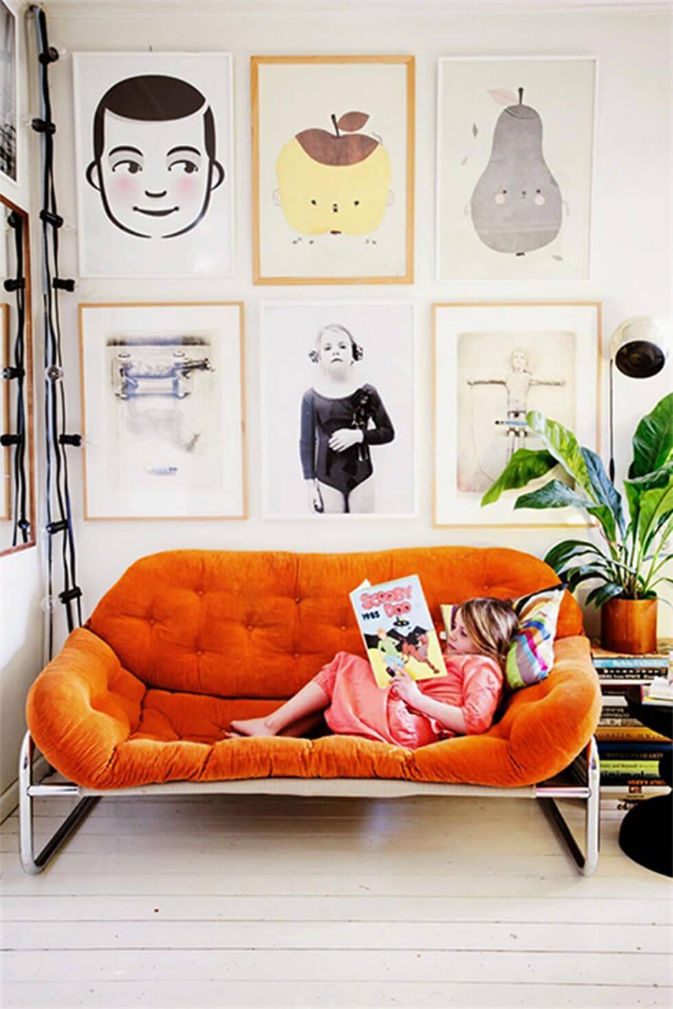 child reading in large orange armchair with big photo frames hanging above