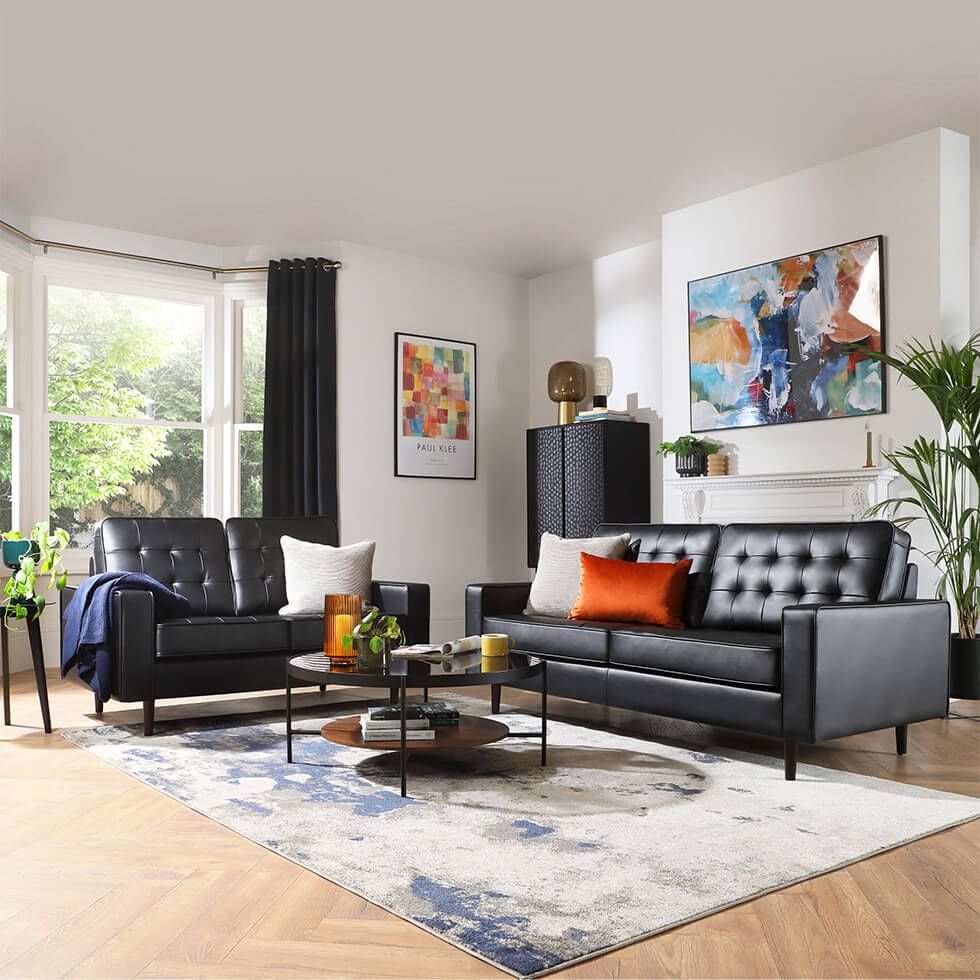 Stylish black leather sofas dressed with jewel tone cushions and throws in a modern living room
