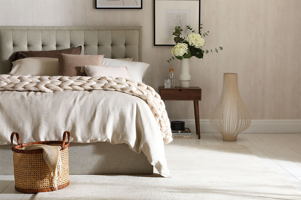 Neutral bedroom with fabric bed, knitted throw and flowers