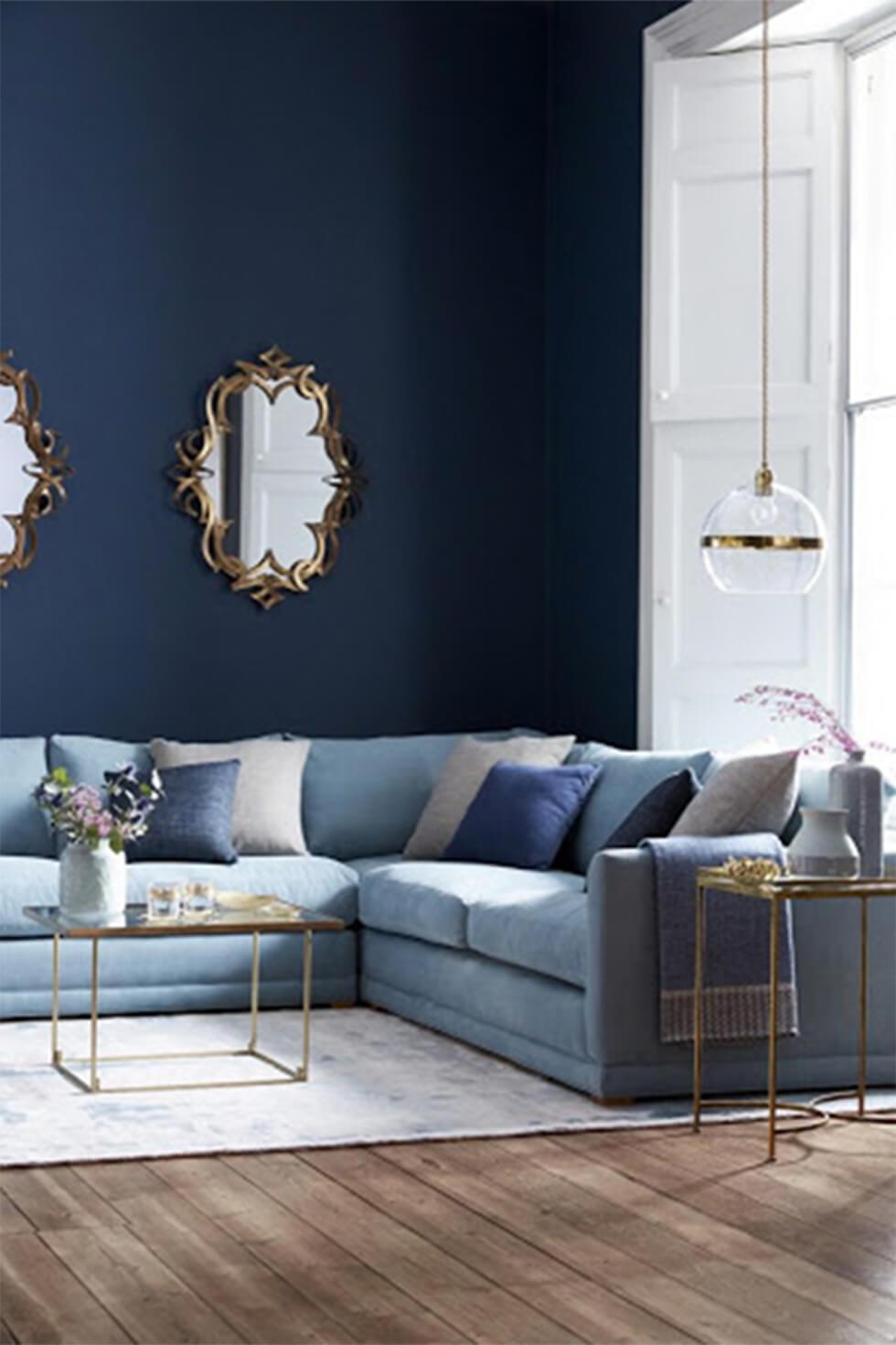Light blue corner sofa in a cosy living room with navy walls.