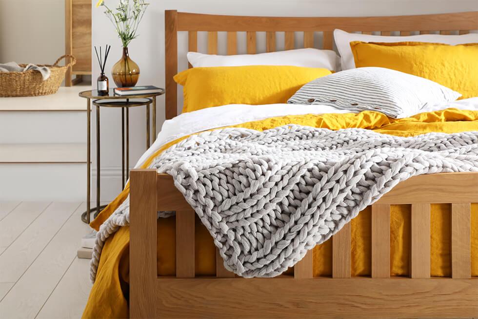 Coastal bedroom with oak bed, yellow bedding and grey knit throw