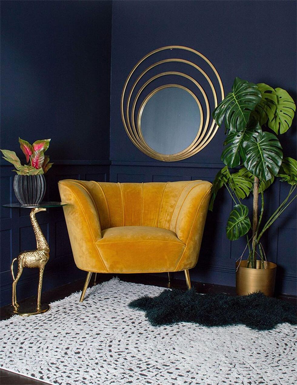 Mustard armchair and gold framed mirror in a deep sapphire blue room