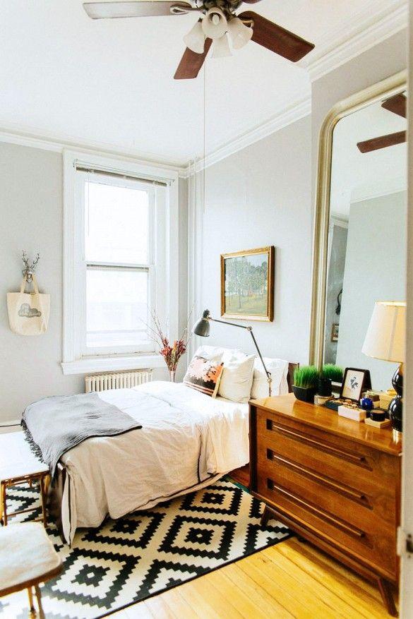 White bedroom with a wooden cabinet, black and white patterned rug, and wooden ceiling fan