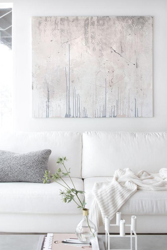 An all-white living room with a white sofa, white knit throw, white side table, and a grey pillow and artpiece.