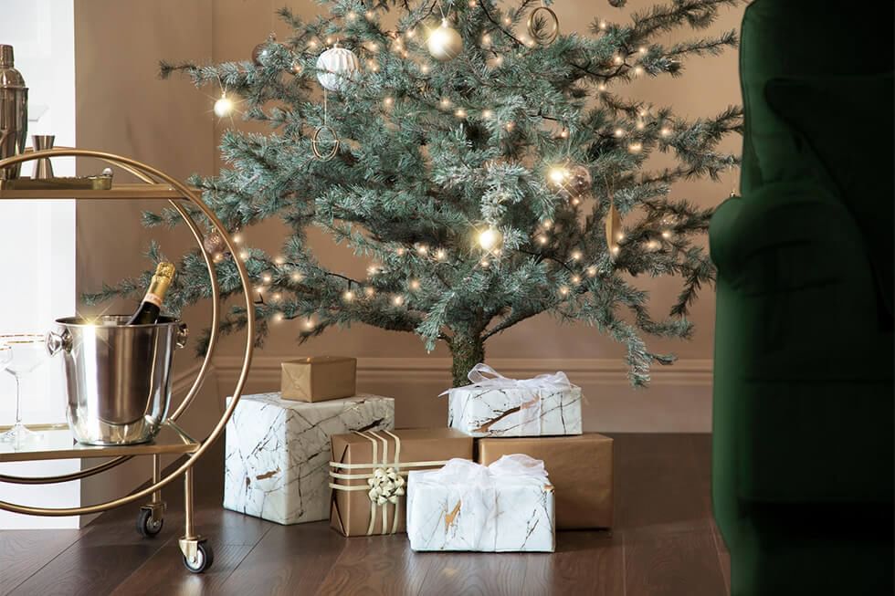 Christmas tree with lights surrounded by presents and bar cart with champagne