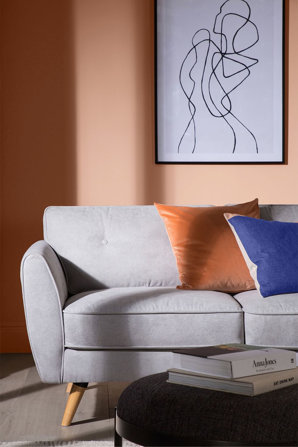A living room with milk chocolate brown walls, bright blue and orange cushions and a light grey sofa