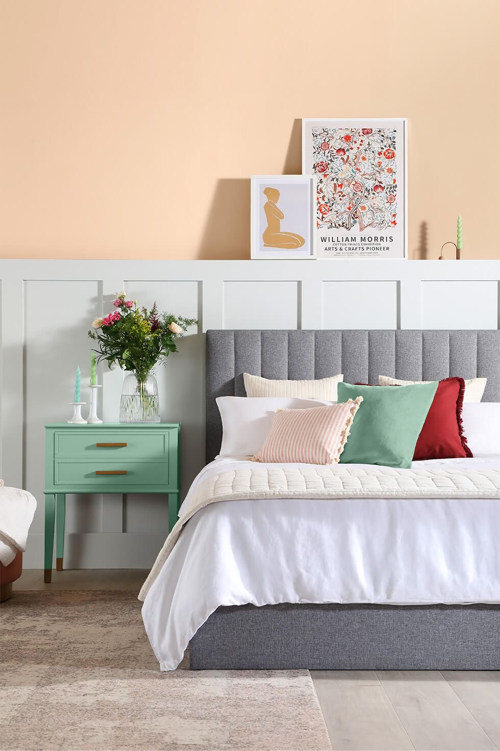 A bedroom with a two-tone peach and white wall, jade green side table and stylish grey fabric bed