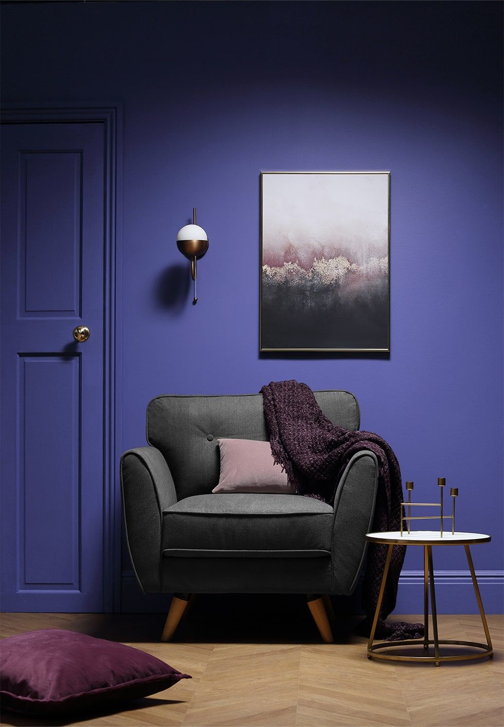 A reading nook with walls painted in Pantone's Colour of the Year 2022 Very Peri and a grey armchair with matching pink cushions.