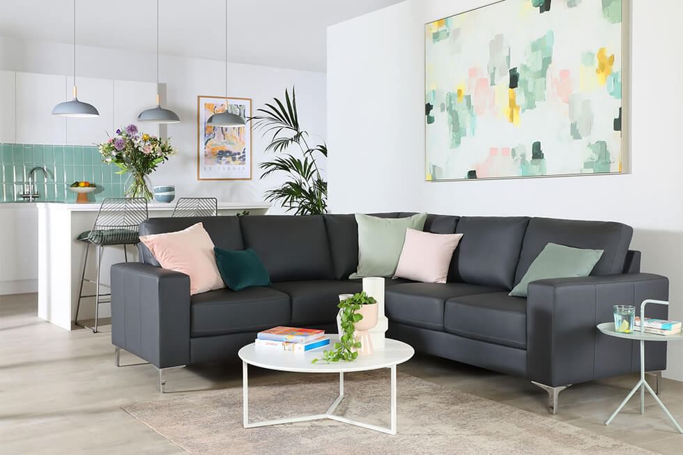 A stylish modern grey leather corner sofa in a white living room with pastel colour accents