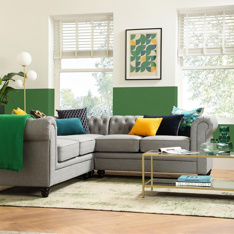 A light grey fabric Chesterfield corner sofa in a contemporary green and white living room