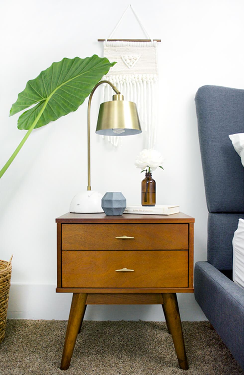 Bedside wooden chest of drawers with splayed legs and a brass lamp