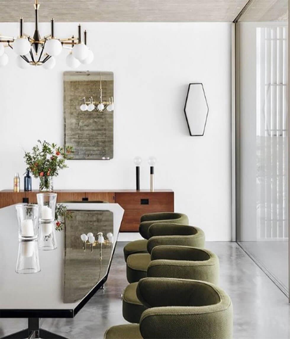 Curved green chairs with uneven shaped table in white dining room with statement lighting