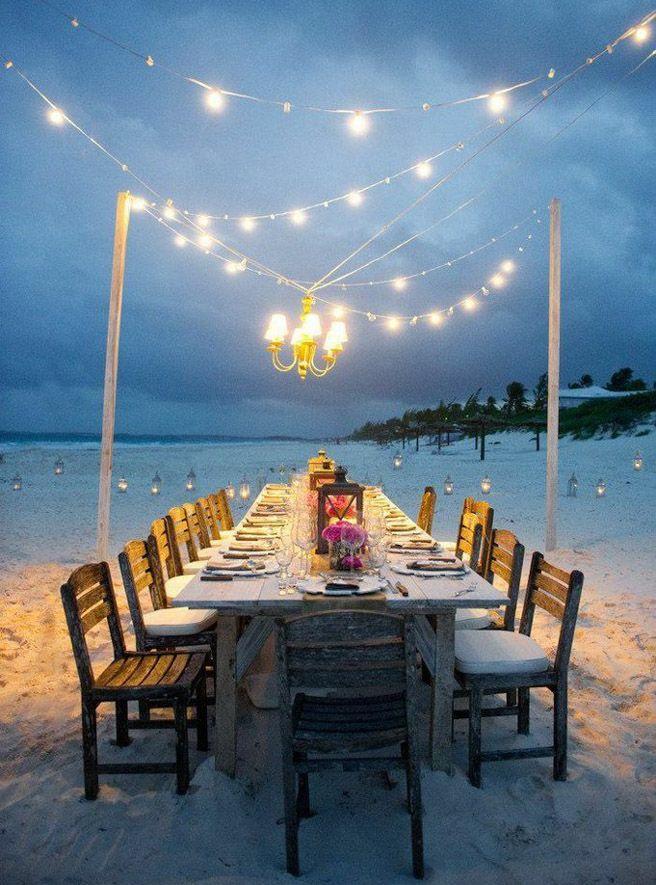 Long dining table by the beach with fairy lights.