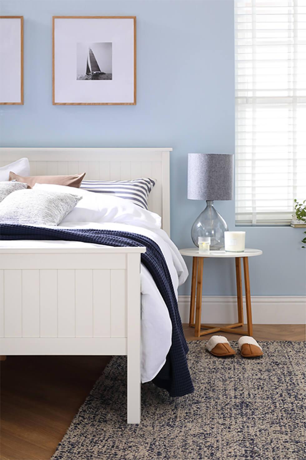 Calm blue bedroom with white wooden bed and framed tie dye art