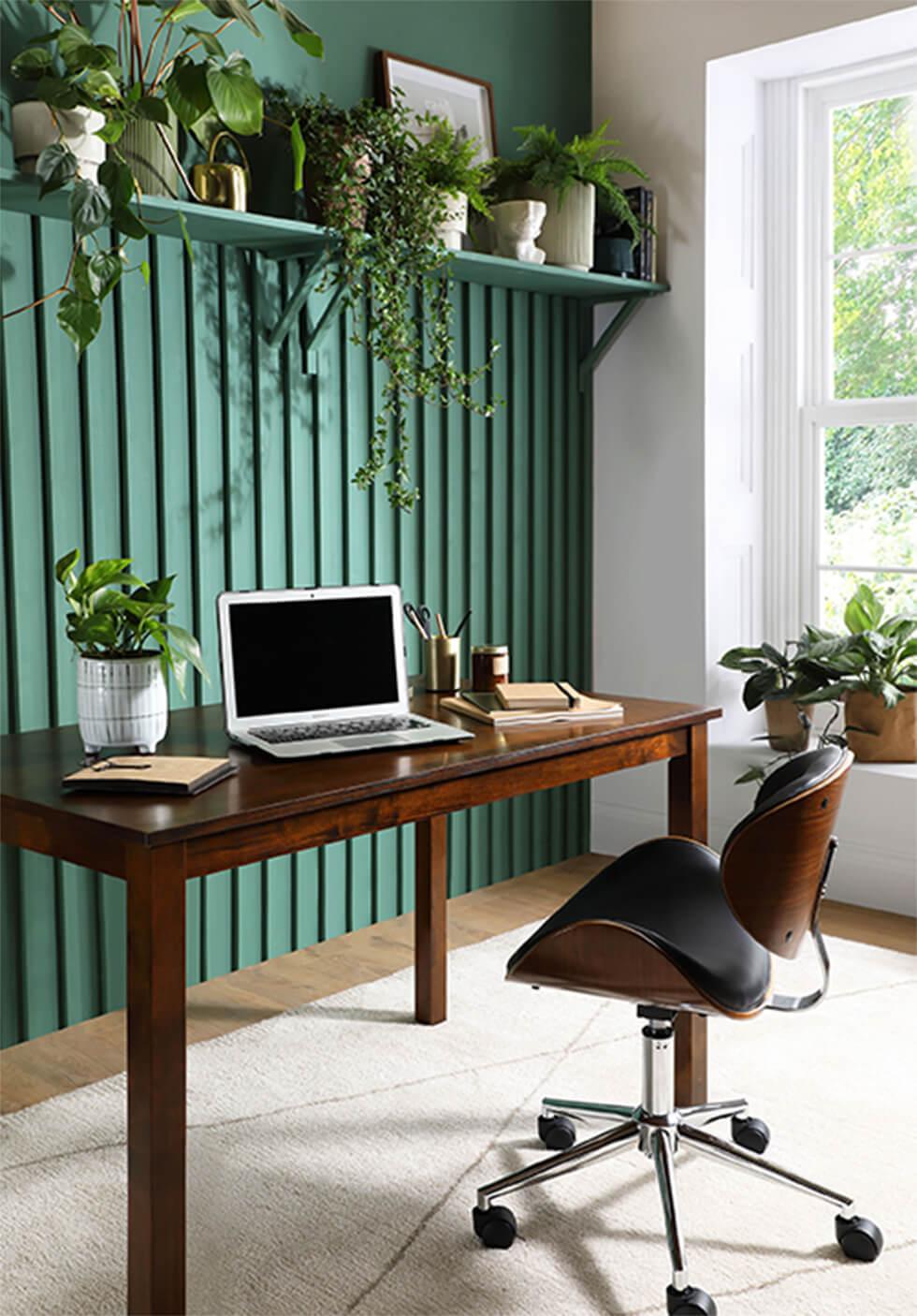 Home office with feature green shiplap wall, indoor plants and dark wood dining table