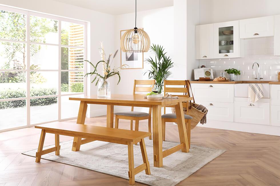 Neutral white dining room with wooden dining table and bench with indoor plants and statement lamp