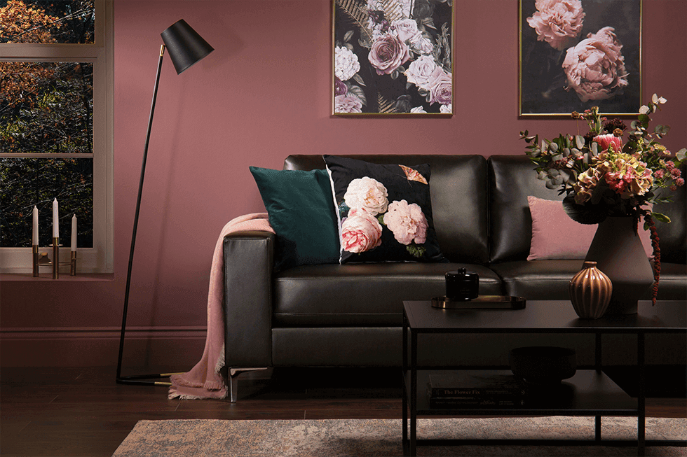 A stylish brown leather sofa paired with pink walls and floral prints