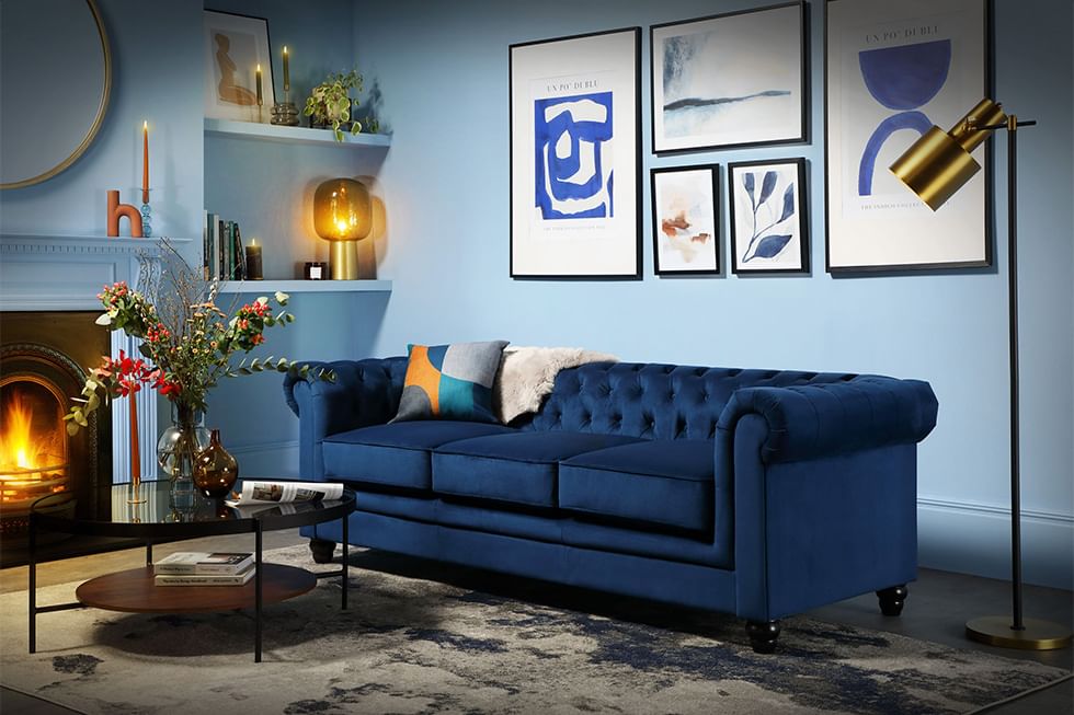 A blue velvet 3 seater Chesterfield sofa in a blue living room