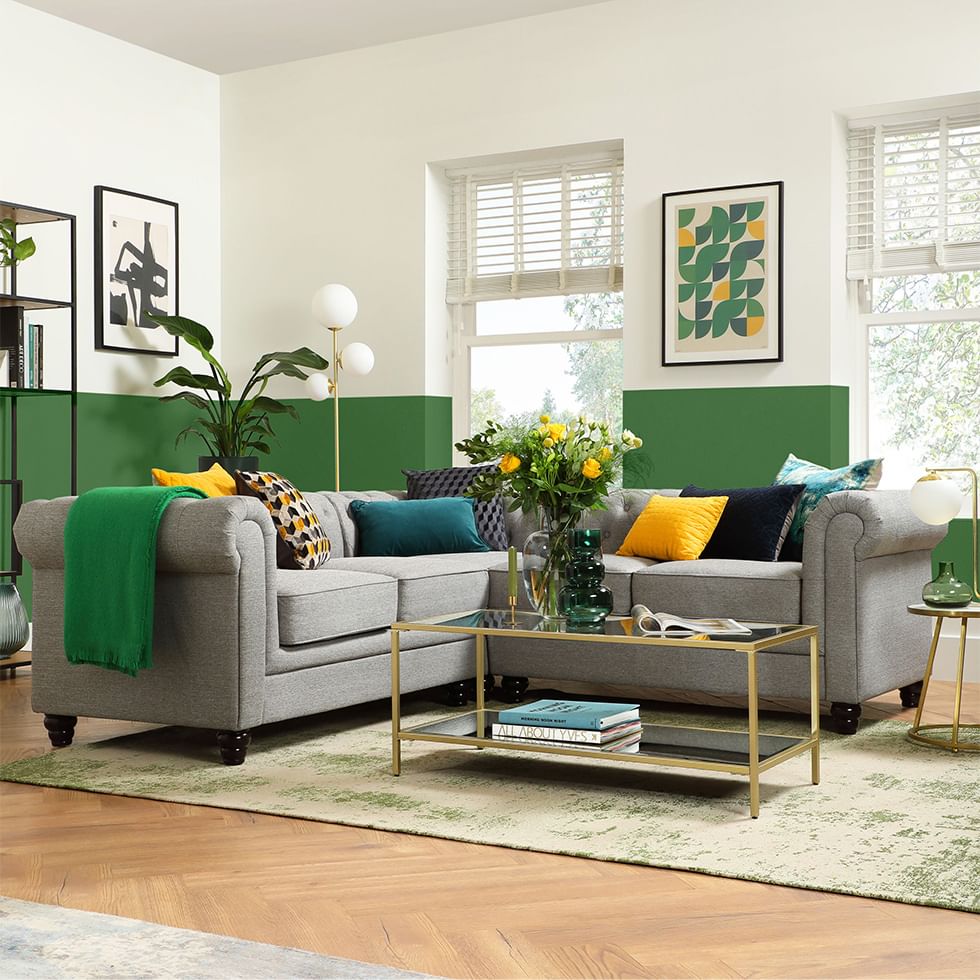 A grey fabric Chesterfield corner sofa in a living room with green and white walls