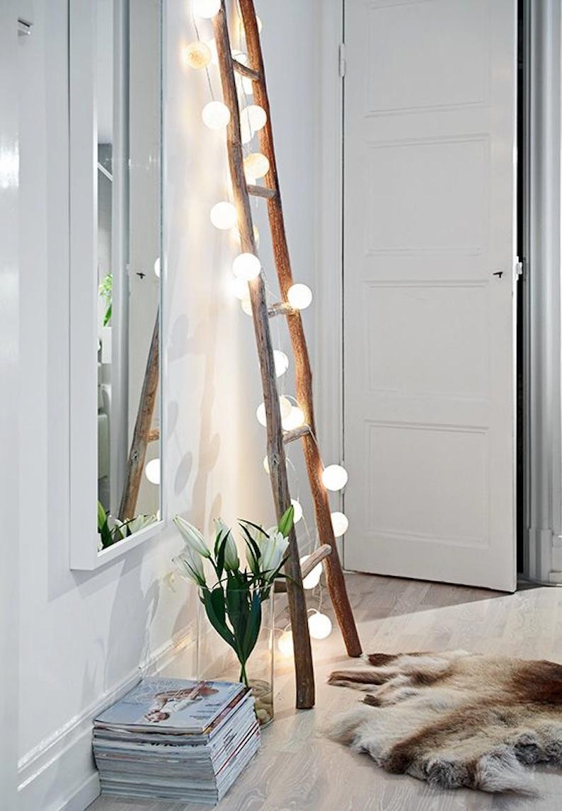 Wooden ladder with lights against a white wall.