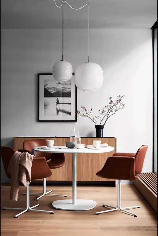 Dining room with white walls, wooden flooring and white table with leather swan chairs.
